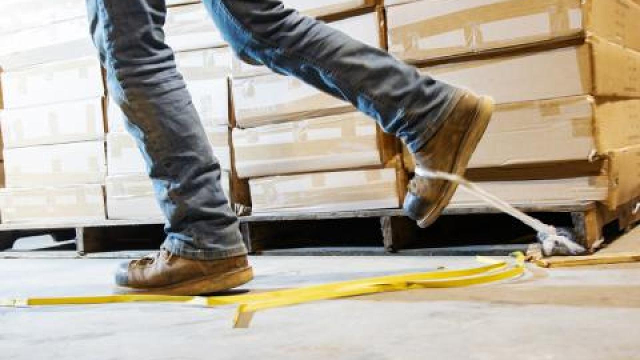 Image of a man about to trip on a strip of tape on a warehouse floor. 