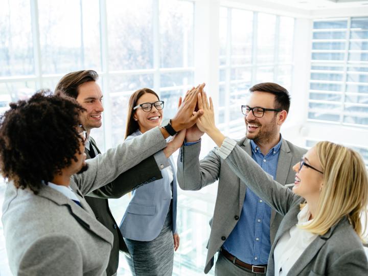 A team of procurement officers high-fives after a successful meeting.