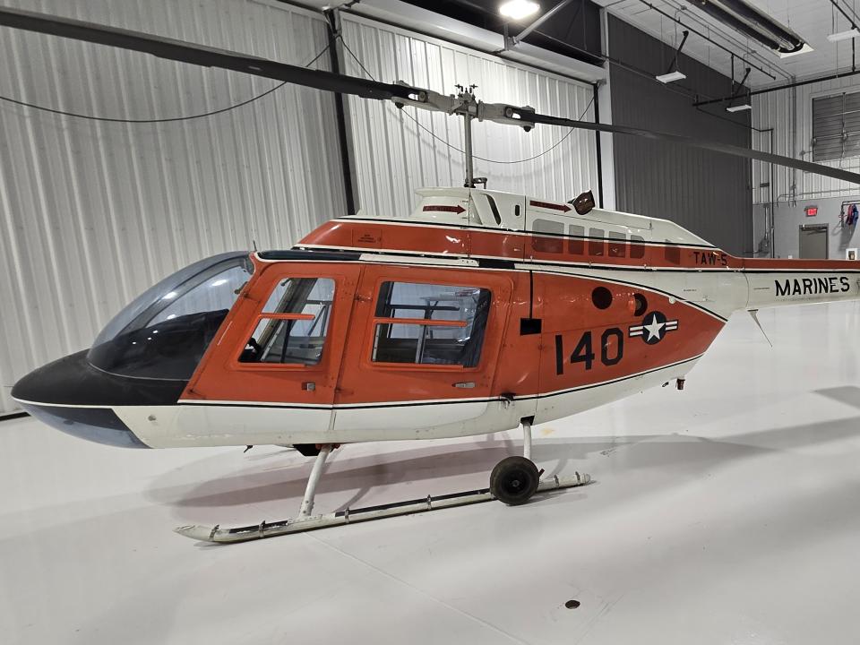 An orange helicopter is parked in a hanger.