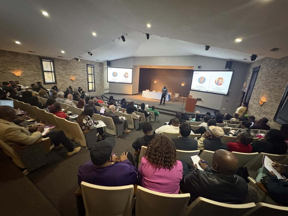 Man stands in far distance on stage speaking to large group in university lecture hall
