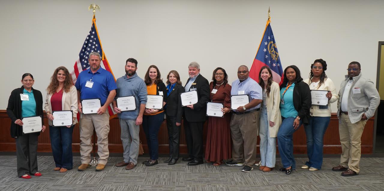 Group of men and women standing in front of USA and Georgia flags