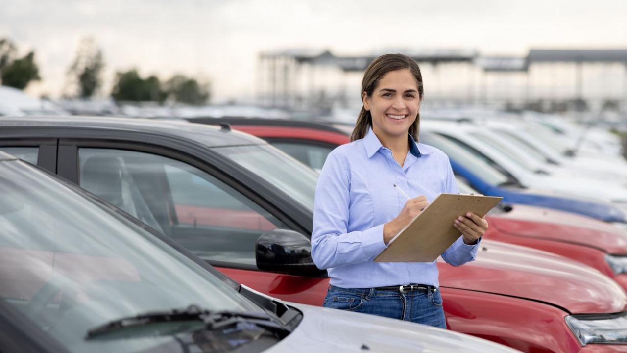 Image of a fleet manager, holding a clipboard, standing amid a row of cars.