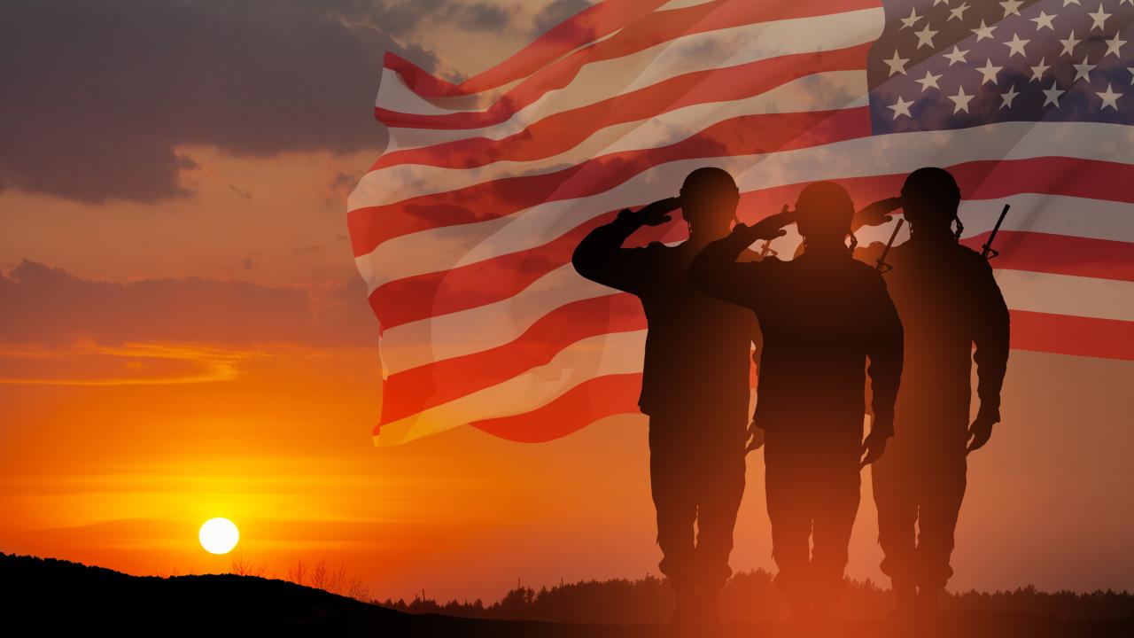 A trio of soldiers, seen only as silhouettes, salute the U.S. flag as the sun sets in the distance., 