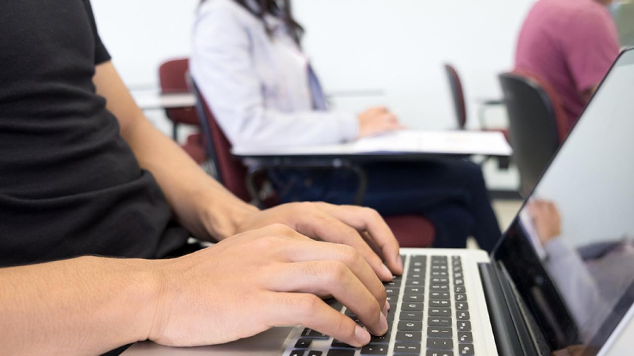 Students in a classroom take notes on laptop computers.