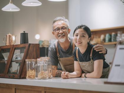 An older Asian man and his daughter stand behind the counter of their bakery.