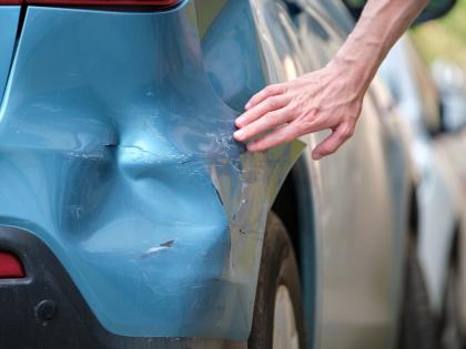 Image of a hand pointing to a damaged car bumper.