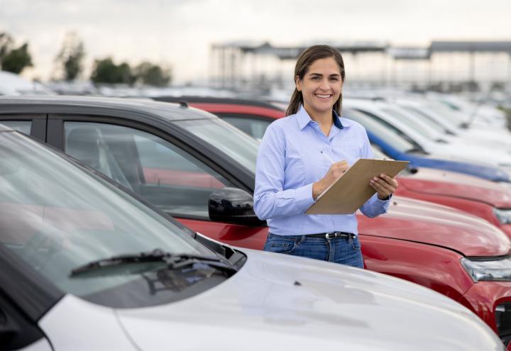Image of a smiling woman with a clipboard reviewing a fleet of cars.