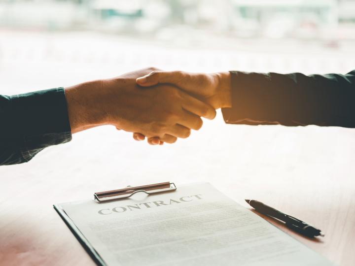 A pair of hands shake over a document labeled &quot;contract.&quot;