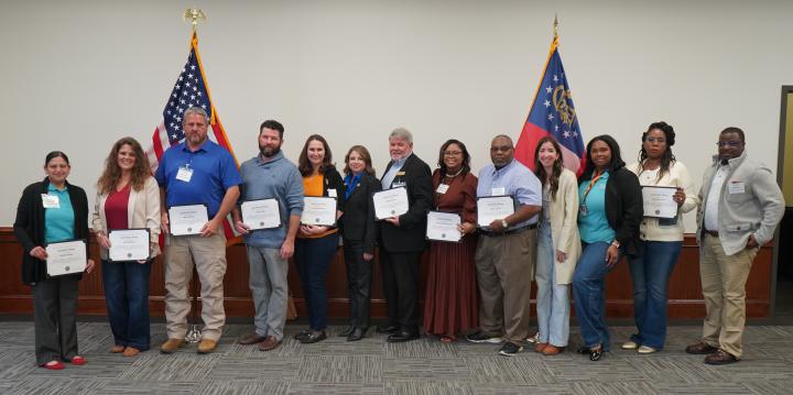 Group of men and women standing in front of USA and Georgia flags