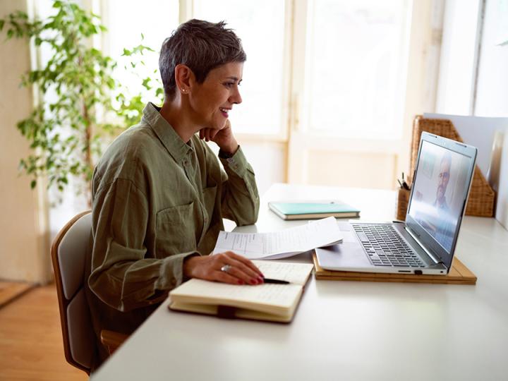 A woman studies at a desk with notebooks and a laptop. 