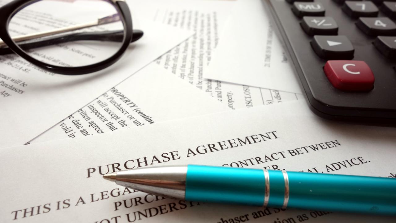 Items on a desk include glasses, a computer keyboard, a pen, and a document labeled, "Purchase Agreement."