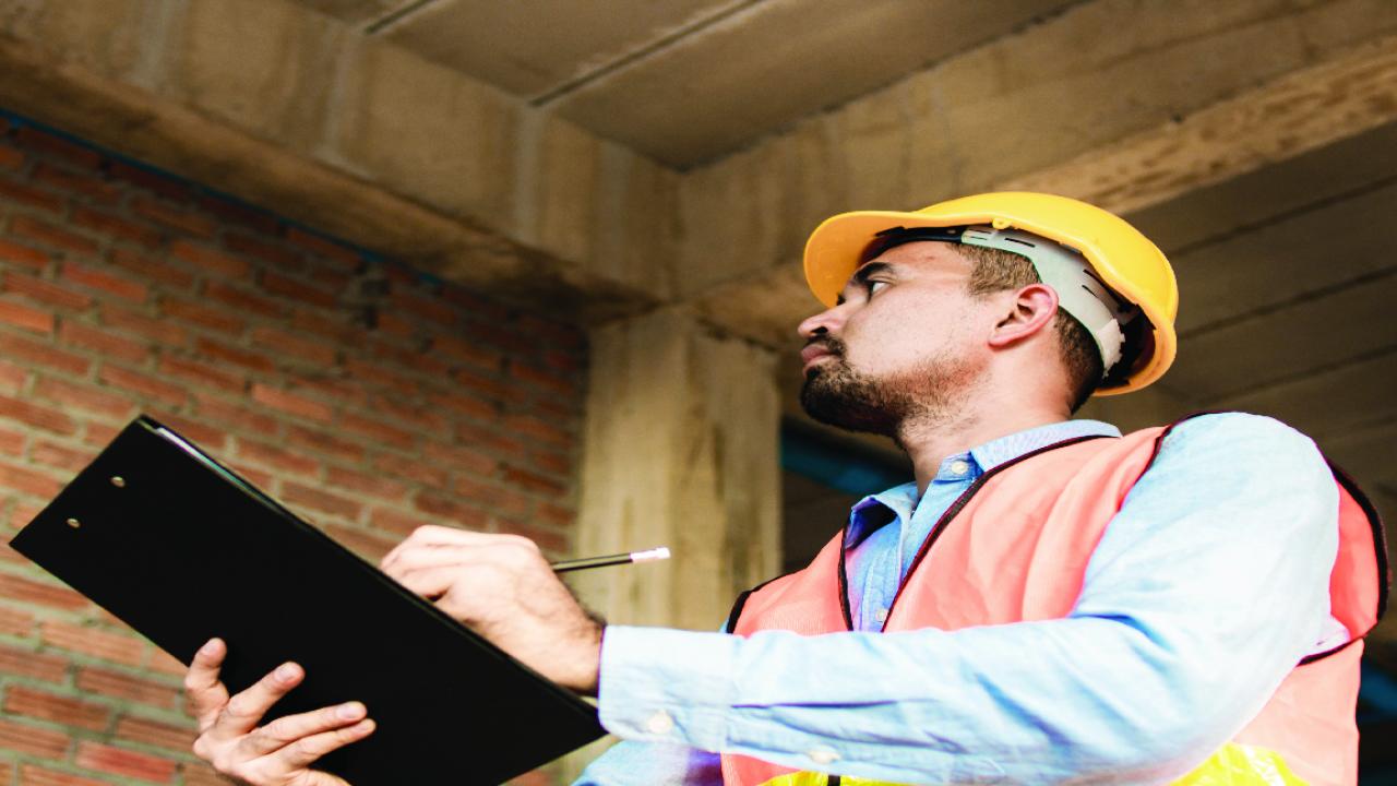 A man weaering a safety vest and carrying a clipboard conducts a building inspection.